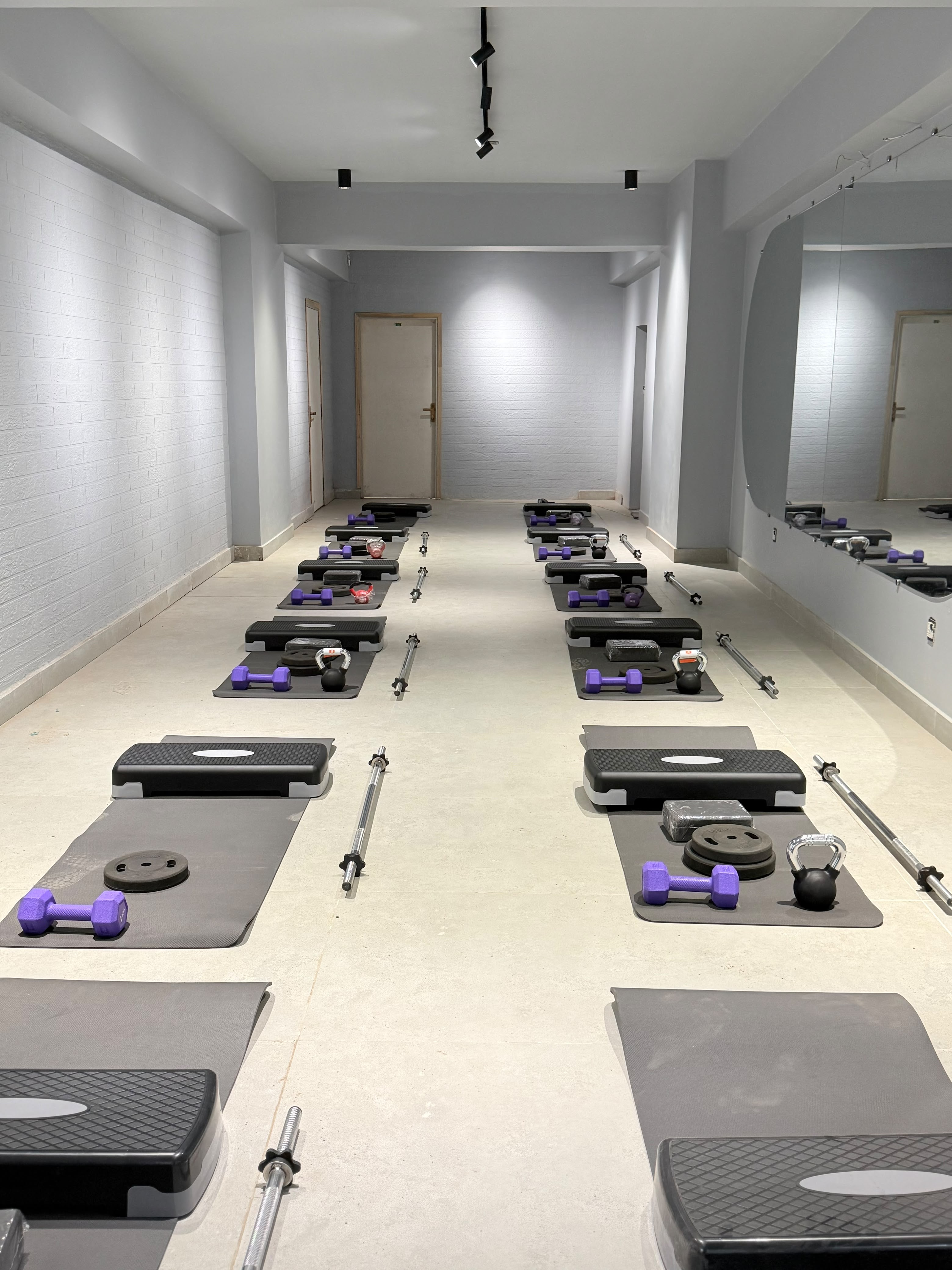 Solace studio stations with mats, barbells, dumbbells and kettlebells, seen from the far end