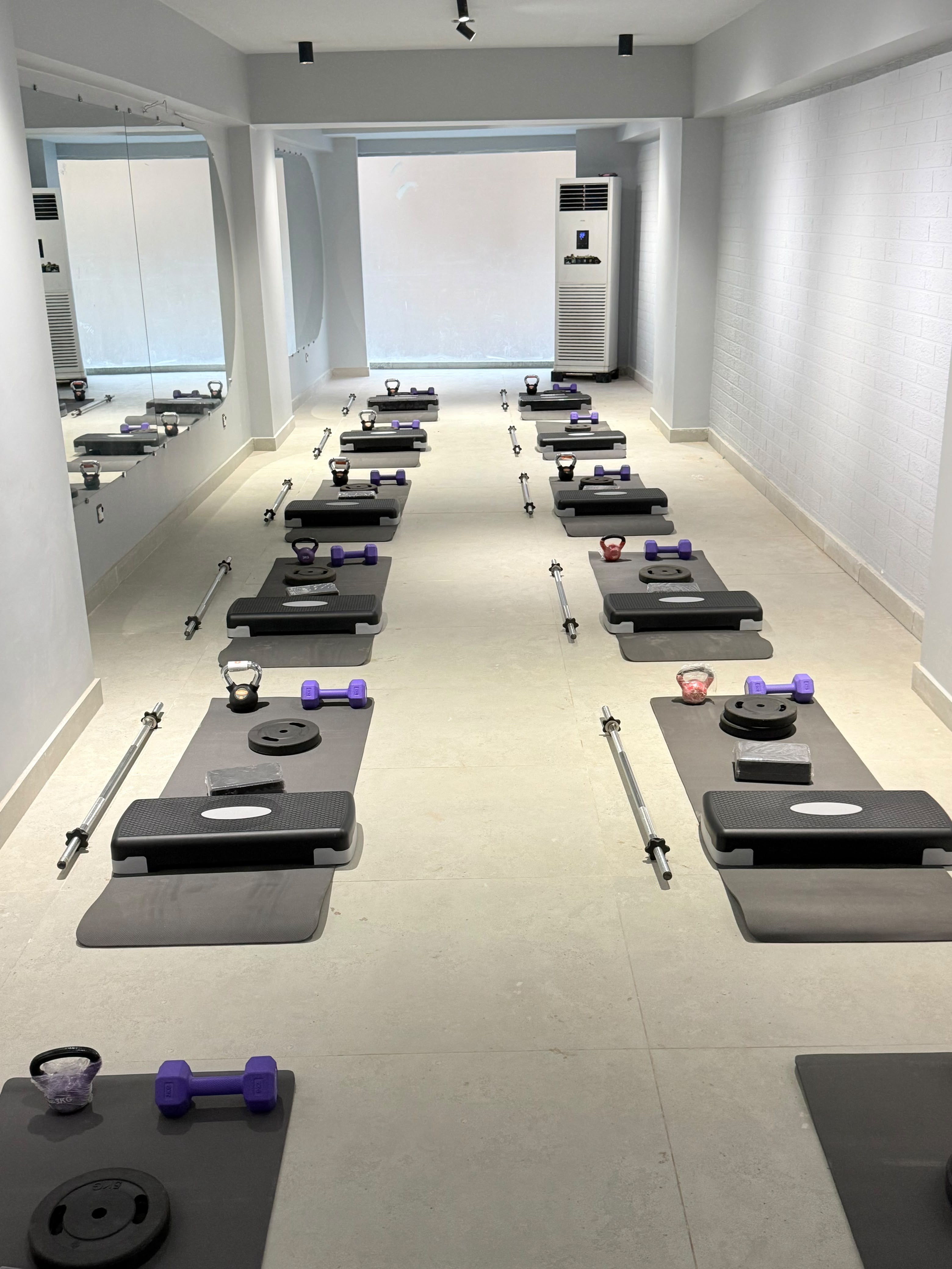 Solace studio with rows of exercise mats, step platforms, purple dumbbells and kettlebells beside mirrored walls