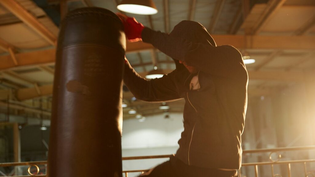 Fighter in a hoodie and red wraps striking a heavy bag during an MMA conditioning session