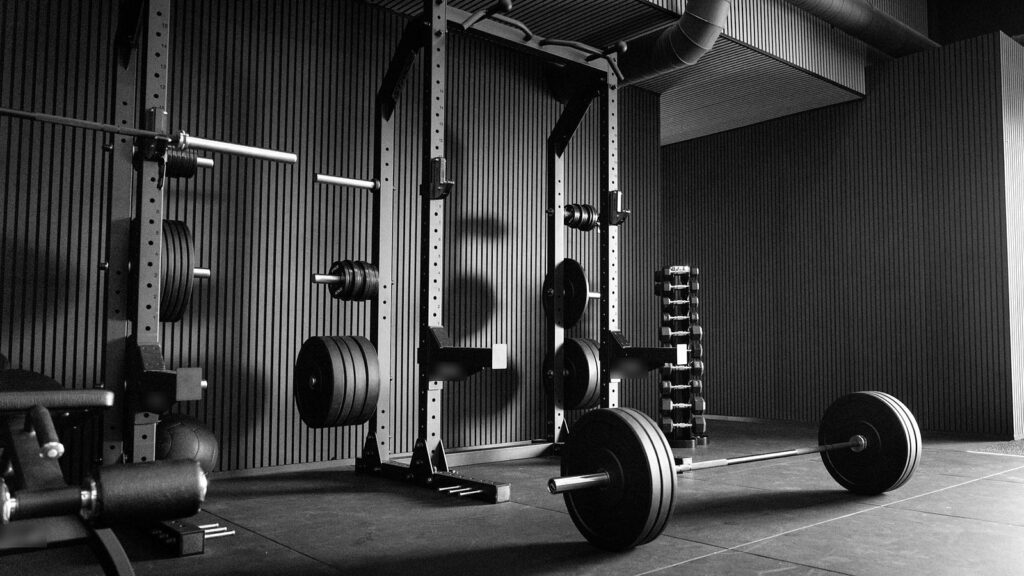 Power racks with weight plates, a dumbbell rack and a loaded barbell on the floor of a strength gym