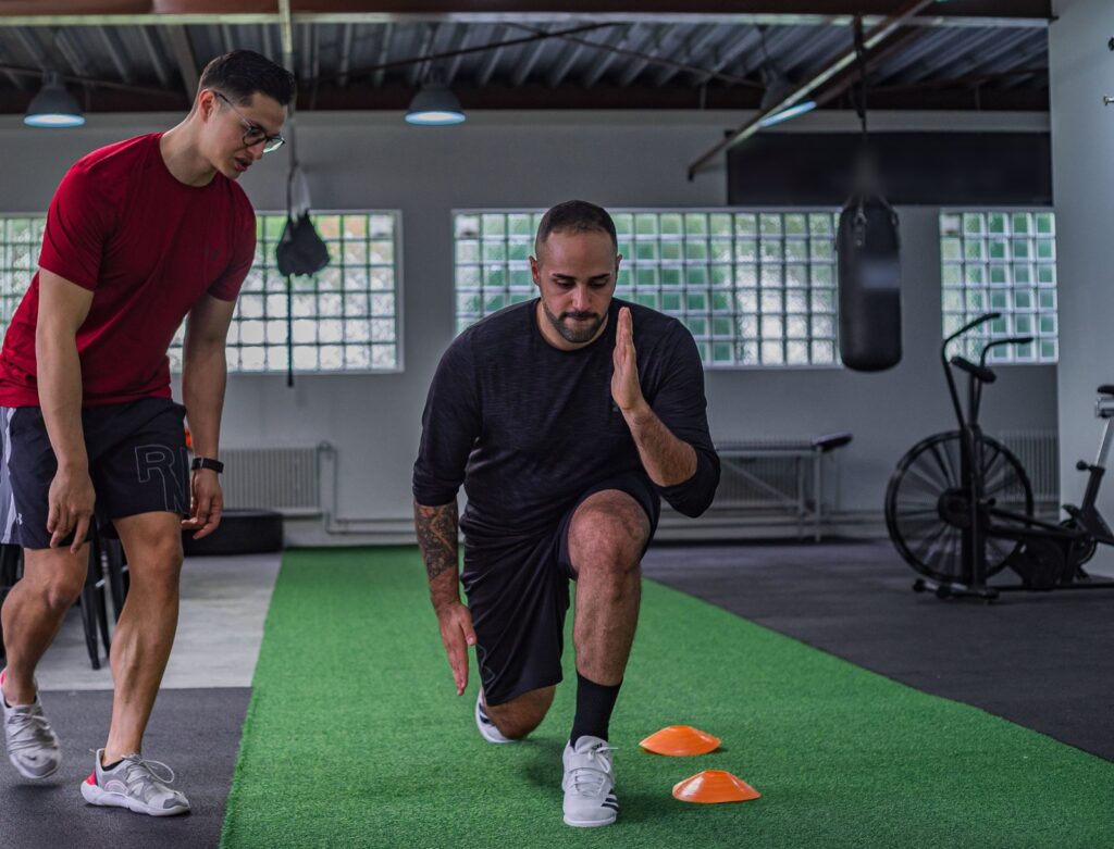 Personal trainer coaching a male client through a lunge drill in a gym