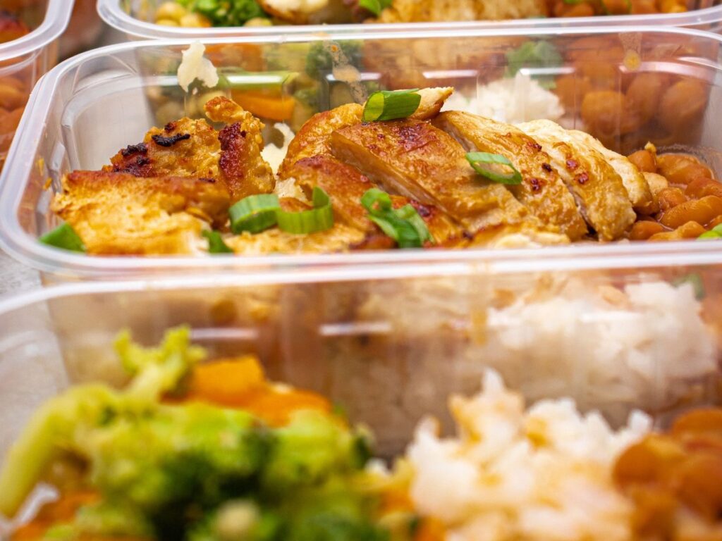 Meal prep containers with grilled chicken, rice, beans and vegetables for after a workout.